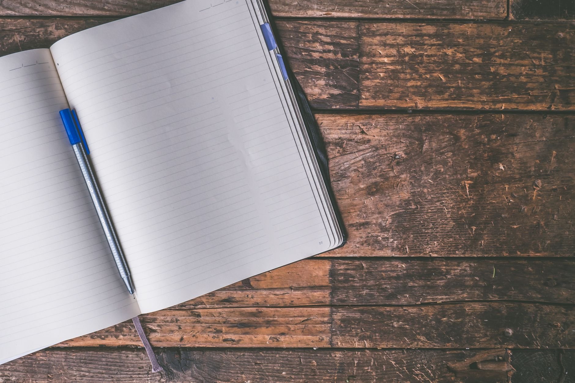 An open notebook with a blue pen on a rustic wooden table, for writing prayers.